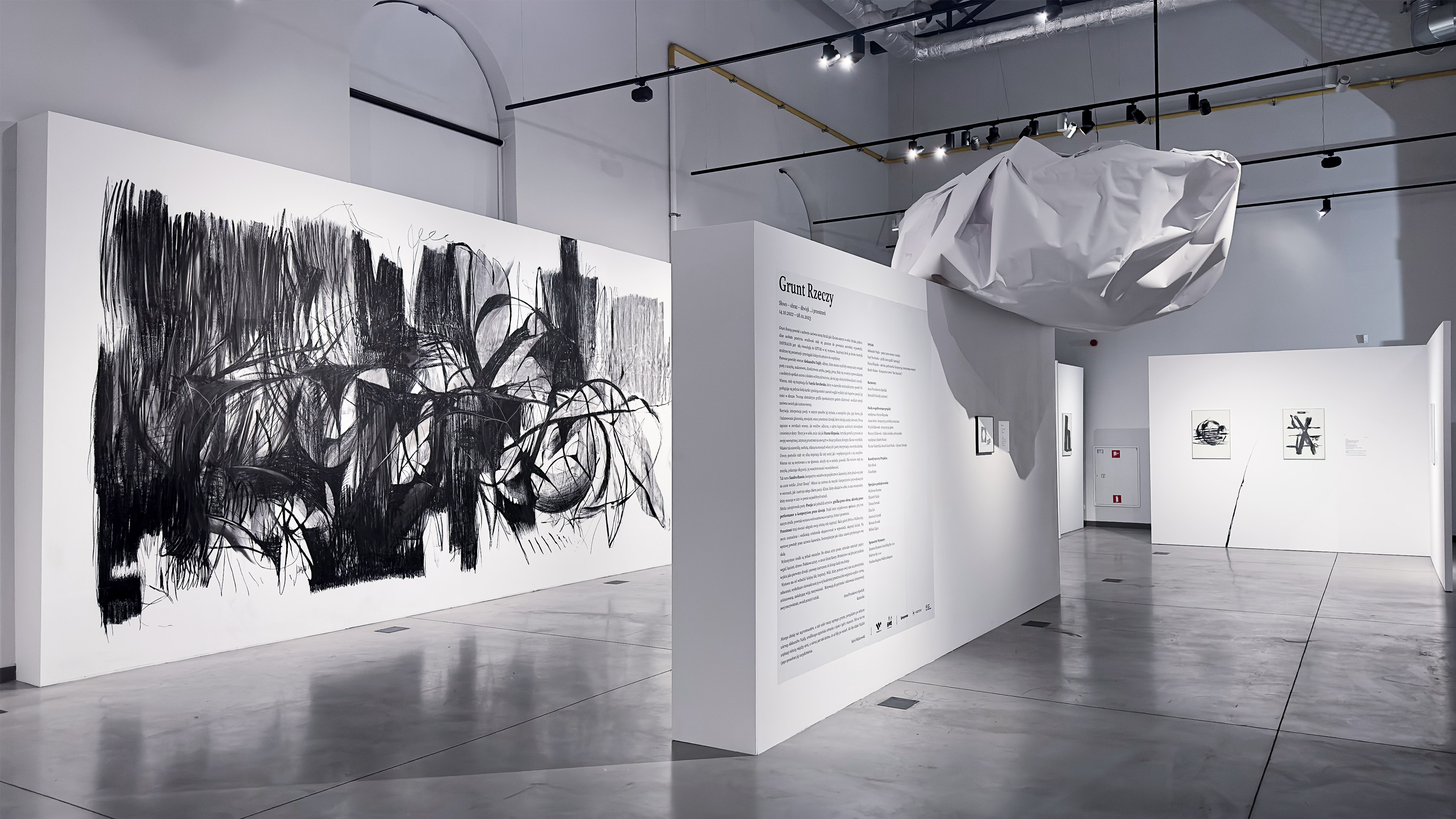 Vasyl Savchenko holds his grandfather by the shoulder in front of the large scale, detailed charcoal drawing of an anthropomorphic form hanging on the wall