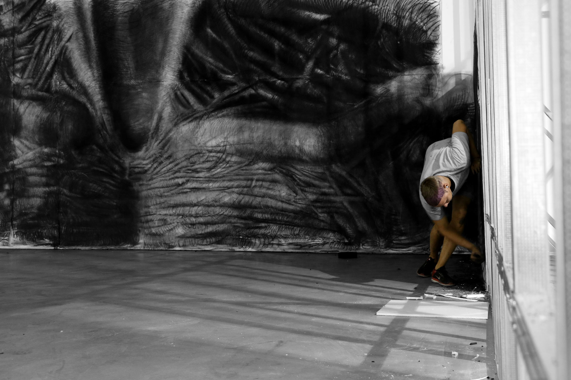 Vasyl Savchenko holds his grandfather by the shoulder in front of the large scale, detailed charcoal drawing of an anthropomorphic form hanging on the wall