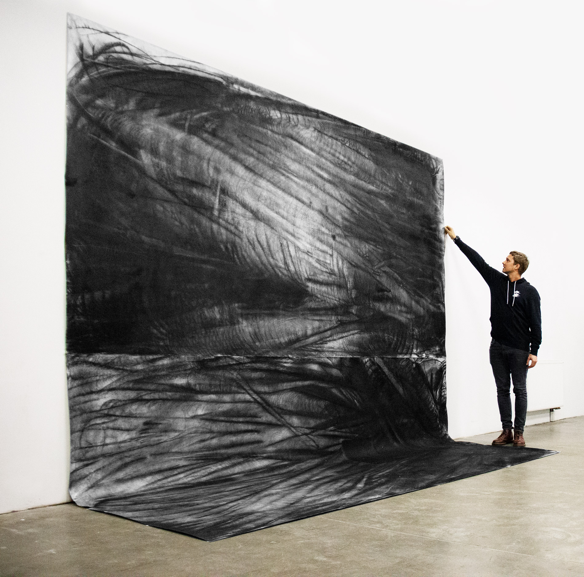 Vasyl Savchenko holds his grandfather by the shoulder in front of the large scale, detailed charcoal drawing of an anthropomorphic form hanging on the wall